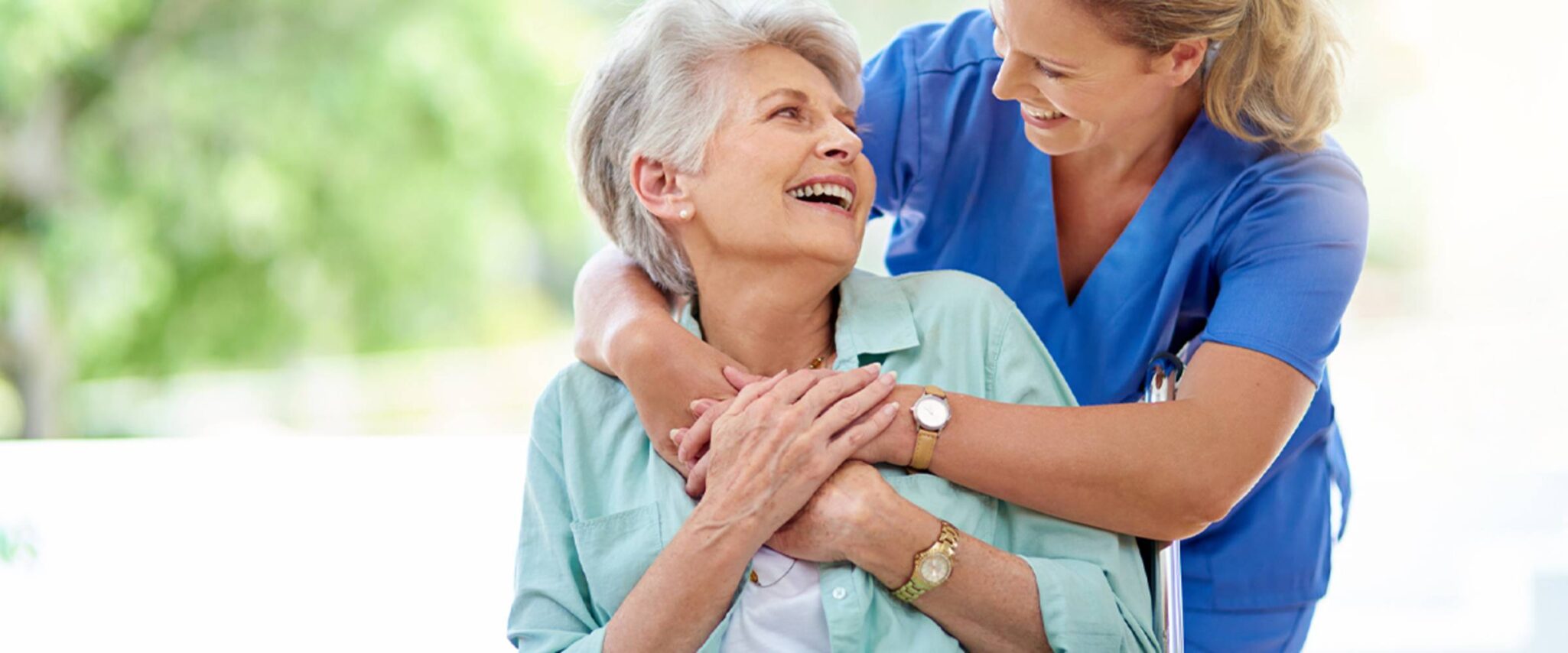 A health care professional hugs a senior woman who is using a wheelchair