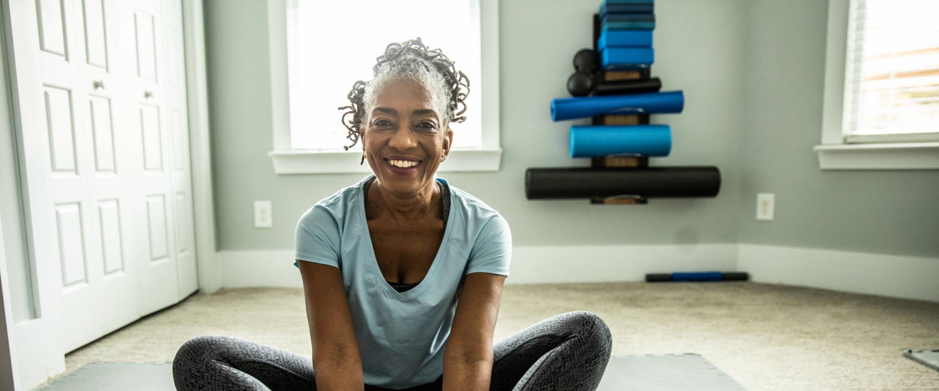 happy senior lady exercising by practicing yoga on a yoga mat in her senior living apartment