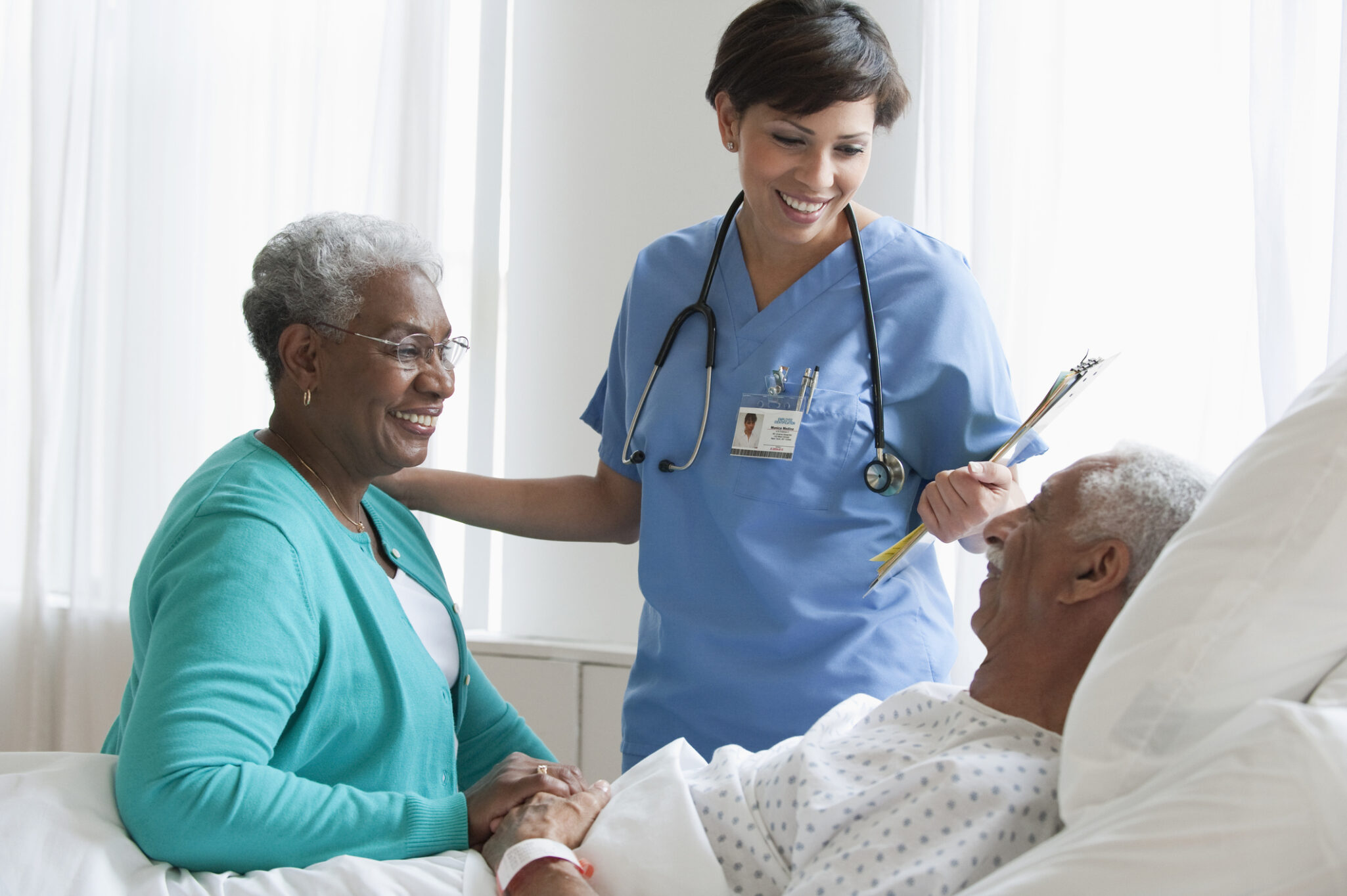 An older man in a hospital bed with his wife beside him an a physician visiting him