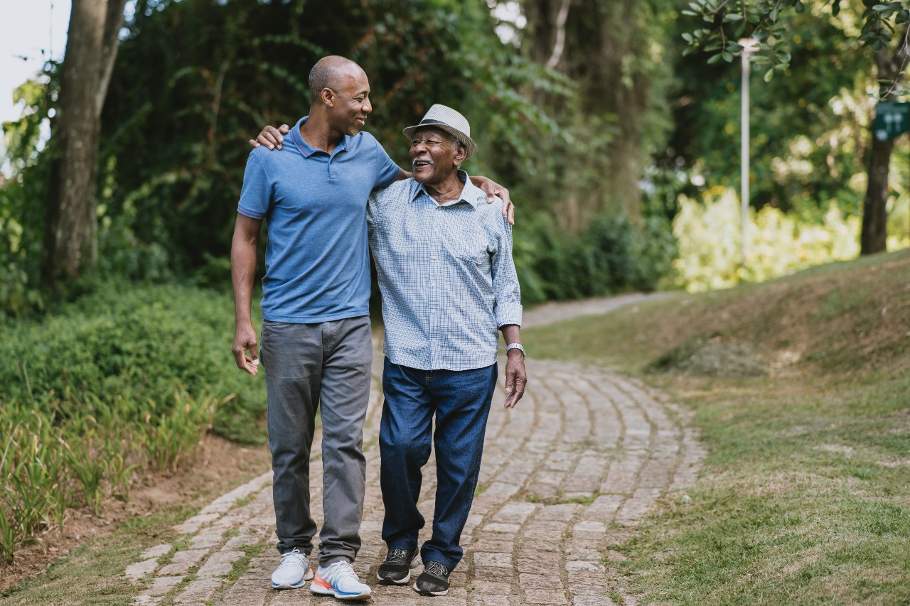 An adult son walks with his senior father on a park path