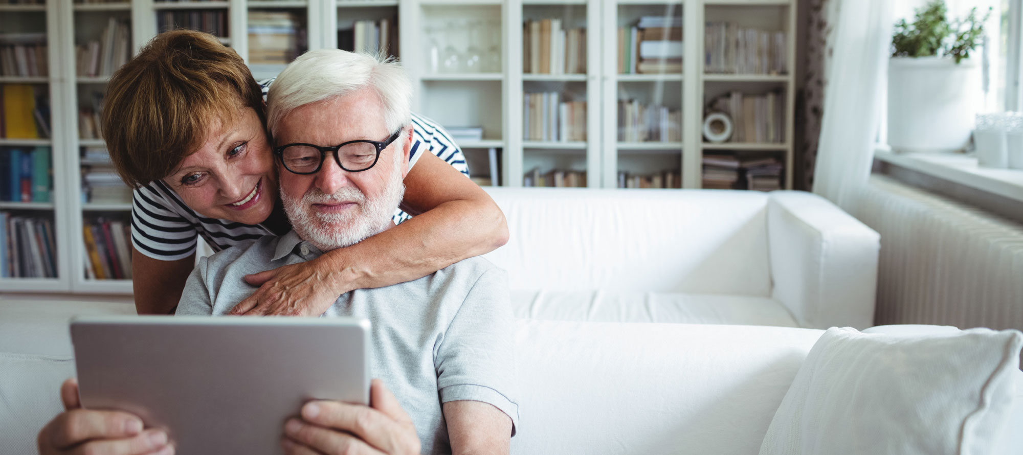 senior wife and husband peer over a tablet together