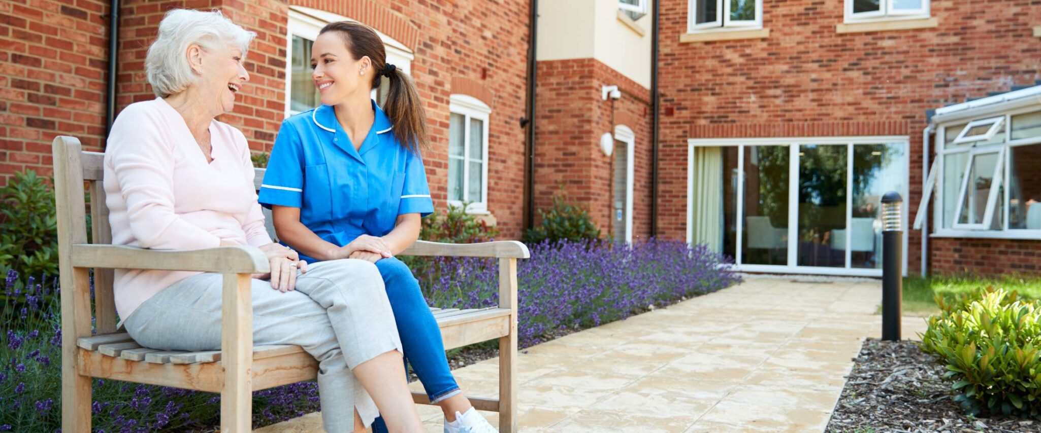 senior and a healthcare worker sitting outside an assisted living facility