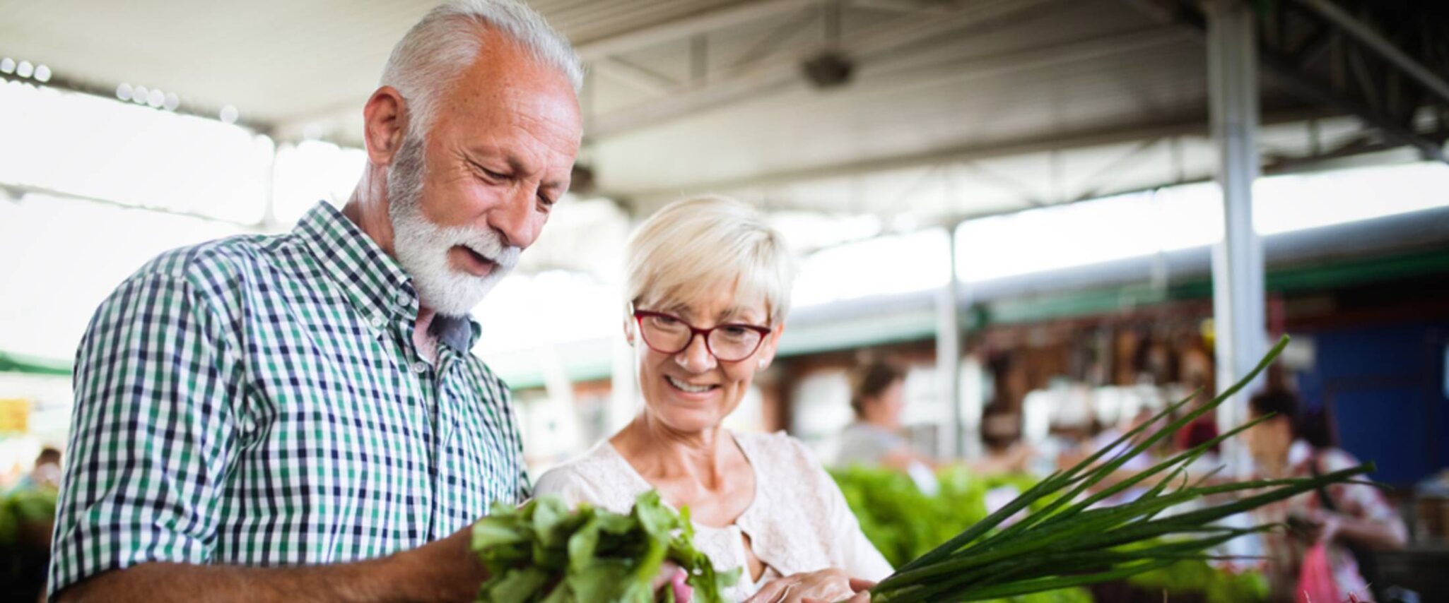 A senior man and woman look at vegetables at a farmer's market.