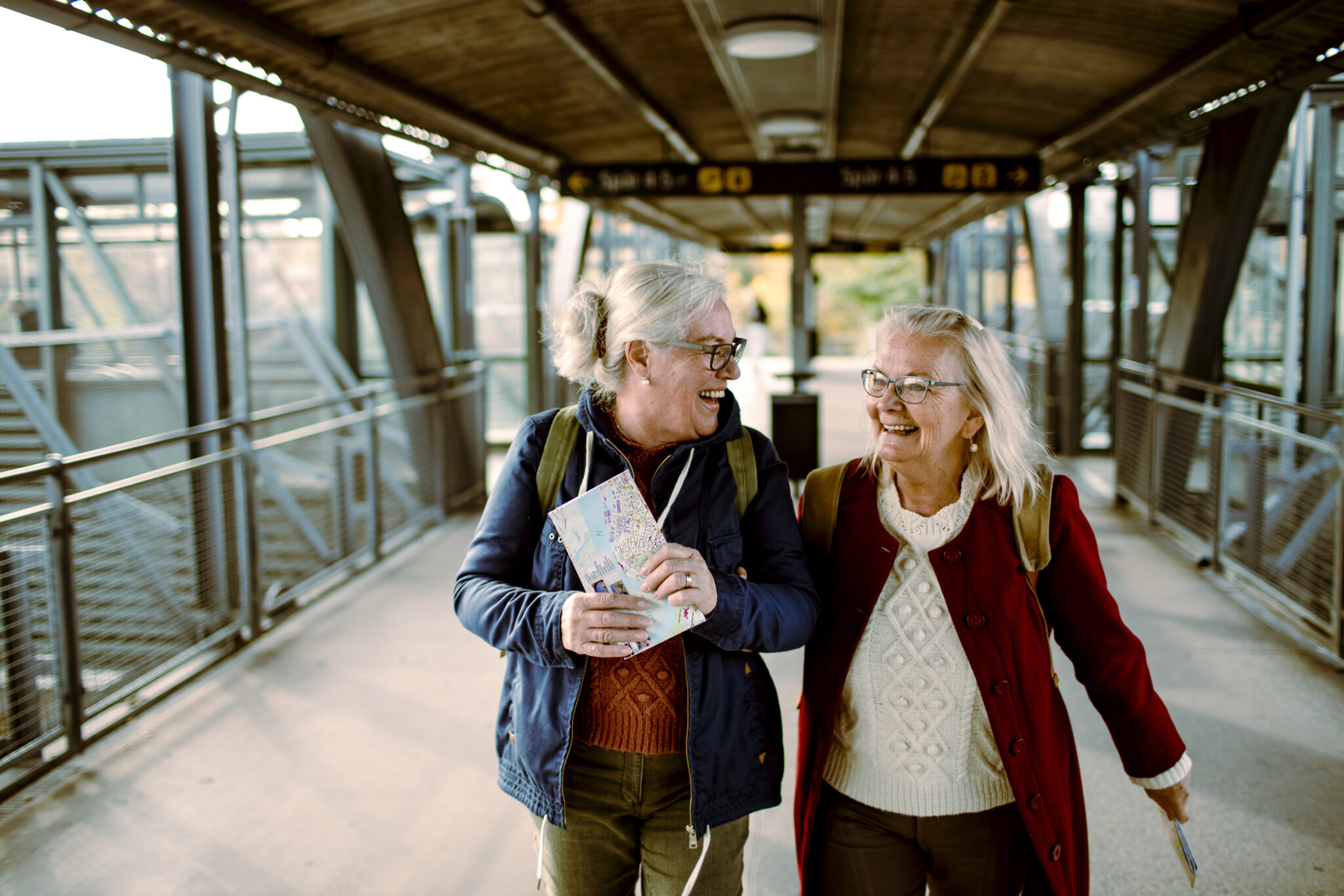 Two older woman in the walkway over the train tracks at a train station