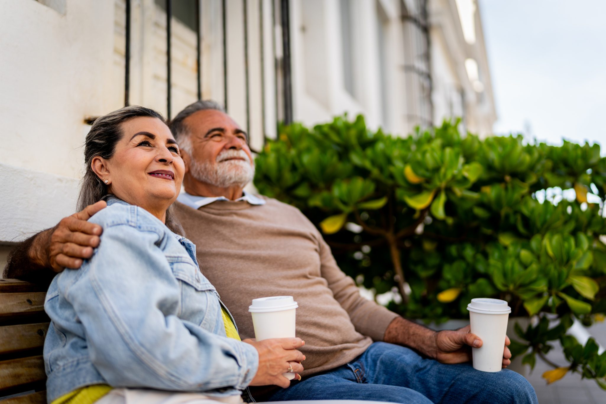 Senior couple sitting on outdoor bench holding coffee cups