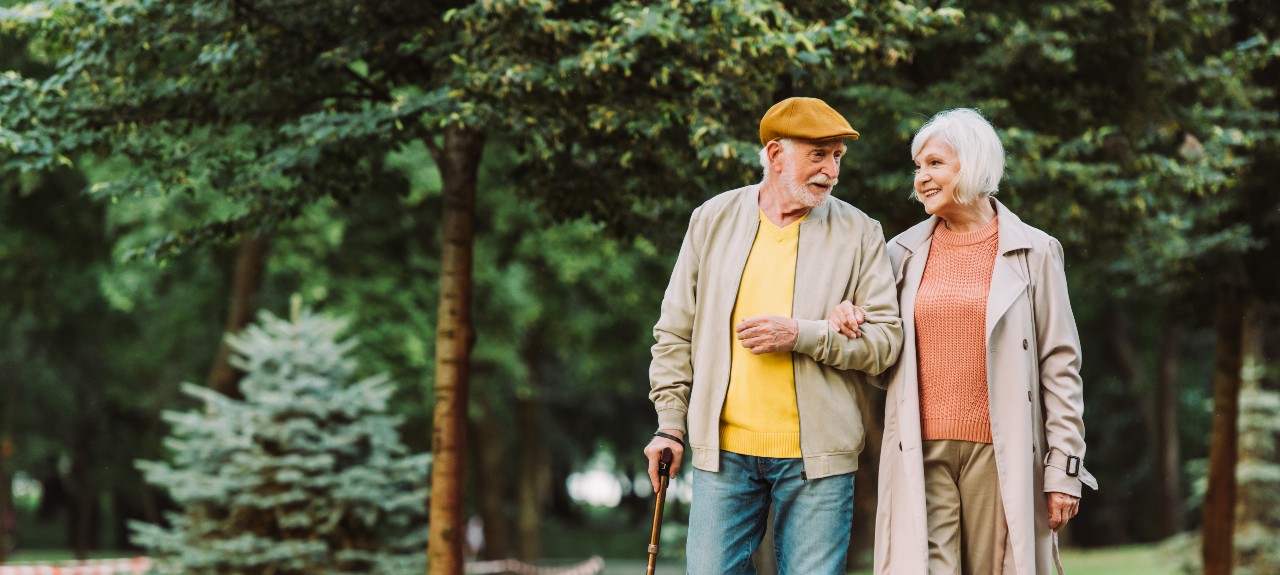 A man with a walking cane and his wife go on a walk in a park
